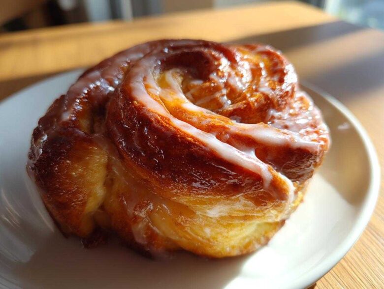 Close-up of a golden brown, freshly baked honey bun with thick white glaze, part of a homemade honey bun recipe.