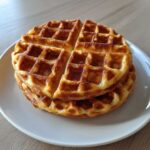 A stack of two golden brown, freshly made easy Belgian waffles on a white plate.