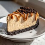 A perfect slice of easy biscoff cheesecake with a dark crust, topped with caramel drizzle and cookie crumbs.