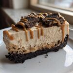 A decadent slice of easy biscoff cheesecake with a dark crust, topped with caramel drizzle and cookie pieces.