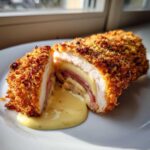 Cross-section of baked chicken cordon bleu showing ham, melted cheese, and creamy sauce oozing out.
