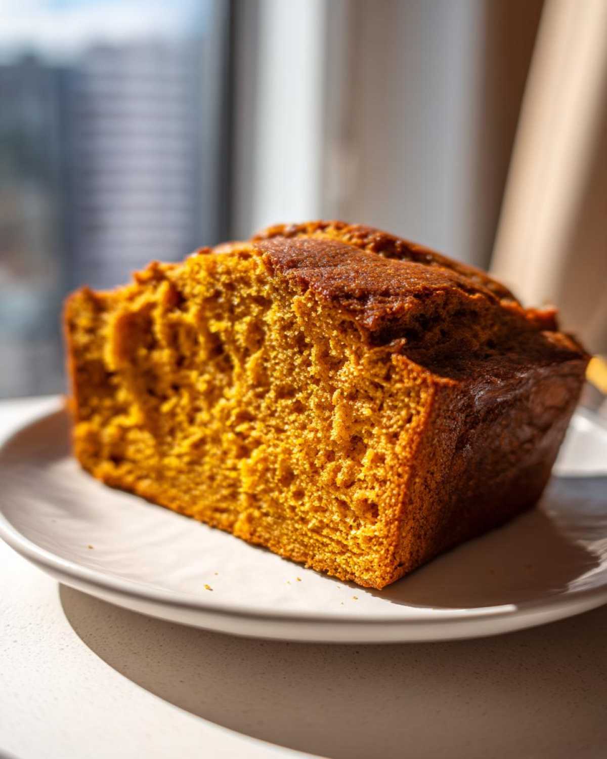 Close-up of a moist slice of easy pumpkin bread with a dark, caramelized crust on a white plate.