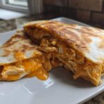 Two halves of a golden-brown buffalo chicken quesadilla showing shredded chicken and melted orange cheese oozing out.