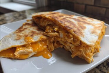 Two halves of a golden-brown buffalo chicken quesadilla showing shredded chicken and melted orange cheese oozing out.