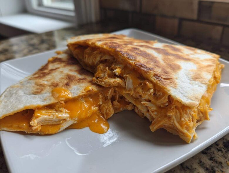 Two halves of a golden-brown buffalo chicken quesadilla showing shredded chicken and melted orange cheese oozing out.
