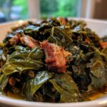 Close-up of tender, seasoned collard greens served in a white bowl with visible pieces of smoked ham hock.