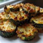 A close-up of several golden-brown, cheesy ovencrisped zucchini slices stacked on a white plate.