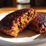 Close-up of a firm black bean burger patty cut in half, showing its texture and dark, caramelized exterior.