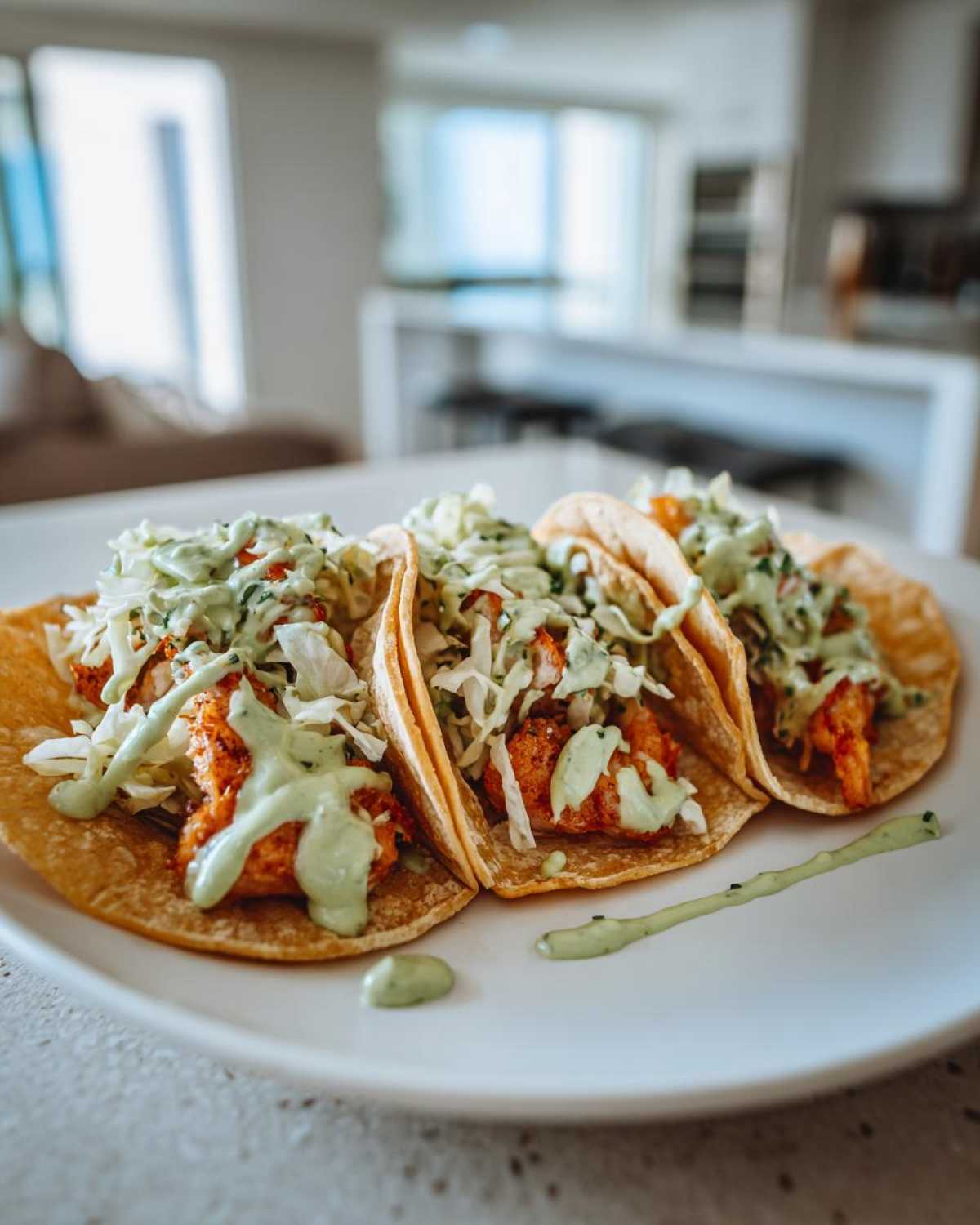 Three fully loaded shrimp taco shells filled with seasoned shrimp, cabbage slaw, and drizzled with green avocado crema.