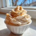 A swirl of fluffy, spiced cinnamon butter piped high in a small white bowl, catching sunlight.