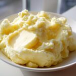A close-up of creamy, fluffy mashed potatoes served in a white bowl, highlighting the smooth texture.