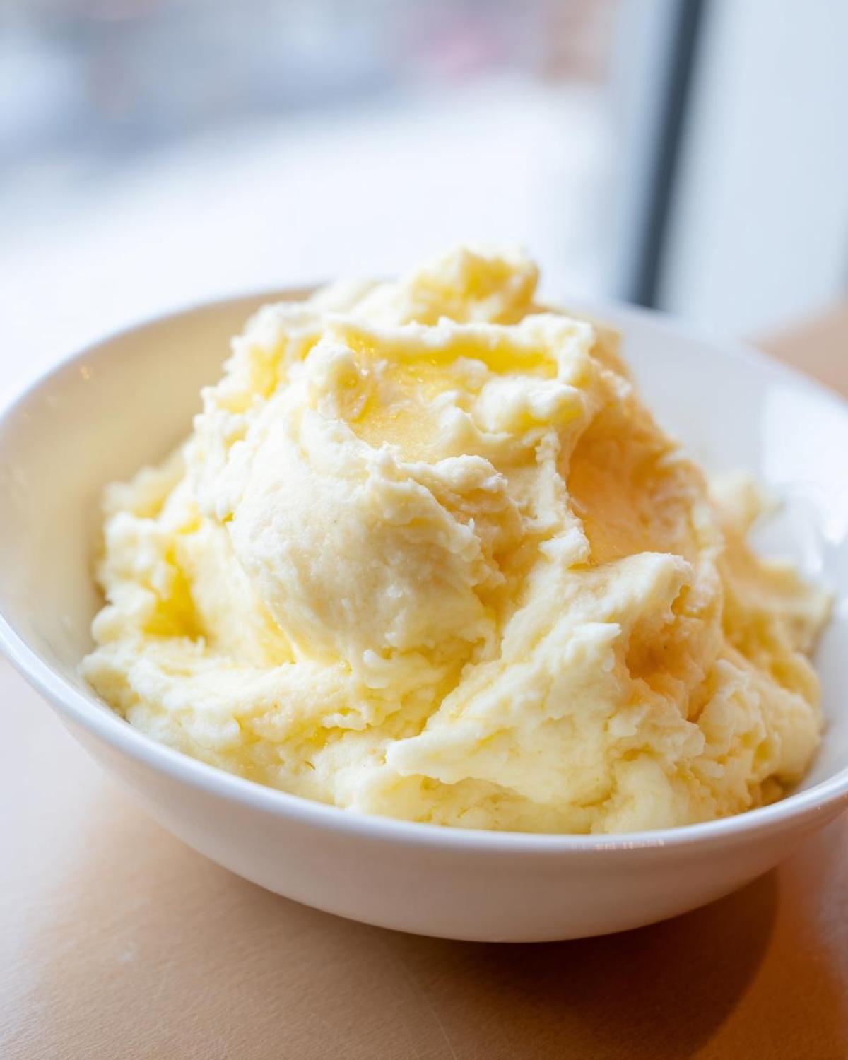 A close-up of a white bowl filled with creamy, fluffy mashed potatoes topped with melted butter.