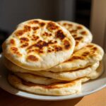 A stack of freshly made, slightly puffed pita bread with golden-brown charred spots.