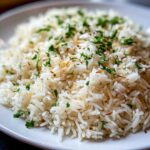 Close-up of fluffy rice pilaf featuring white rice, toasted brown vermicelli, and chopped green parsley garnish.