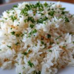 Close-up of a mound of fluffy white rice pilaf garnished with chopped green parsley and small brown crispy bits.