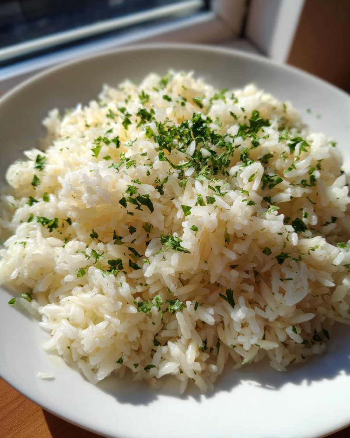 Close-up of a white bowl filled with fluffy rice pilaf, garnished generously with chopped fresh parsley.