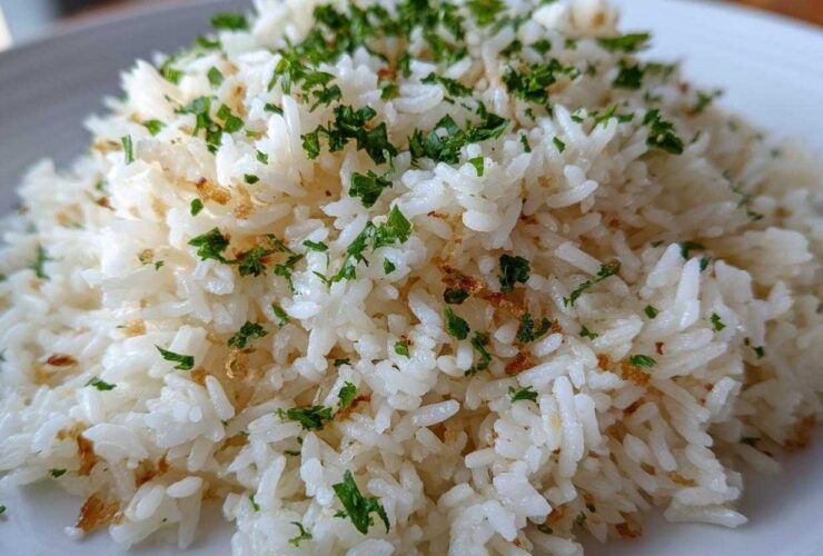 Close-up of a mound of fluffy white rice pilaf garnished with chopped green parsley and small brown crispy bits.