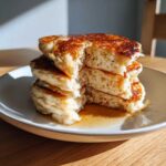 Close-up of a stack of fluffy sourdough discard pancakes, cut open to show the airy interior, drizzled with maple syrup.