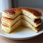 A stack of three thick, fluffy sourdough discard pancakes, cut to show the airy interior, drizzled with syrup.