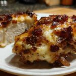 Two pieces of juicy french onion chicken, topped with melted cheese and caramelized onions, served on a white plate.
