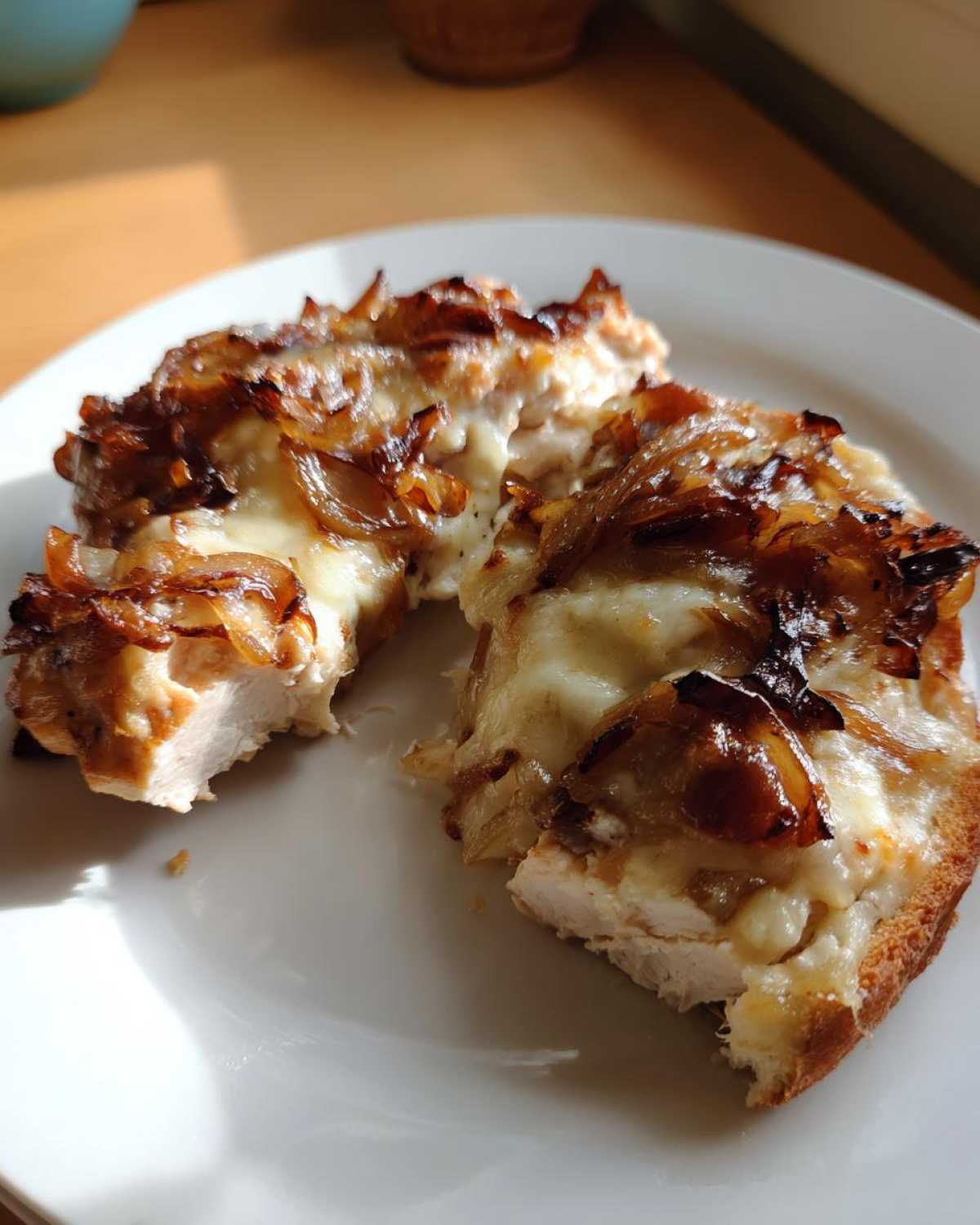 Two pieces of juicy french onion chicken topped with melted cheese and caramelized onions on a white plate.