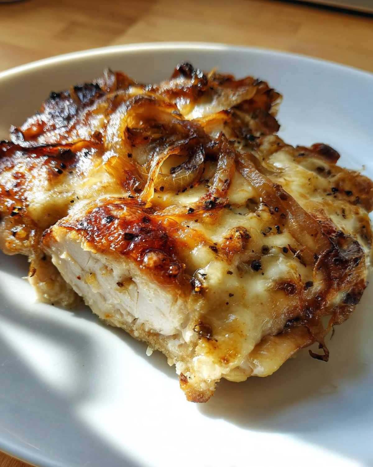 Close-up of a perfectly cooked piece of french onion chicken showing the moist white meat inside and cheesy, caramelized onion topping.