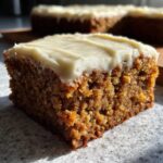 A close-up shot of a moist square slice of Frosted Zucchini Spice Bars with thick cream cheese frosting.