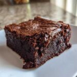 A close-up of a fudgy, rich, dark chocolate greek yogurt brownies square on a white plate.