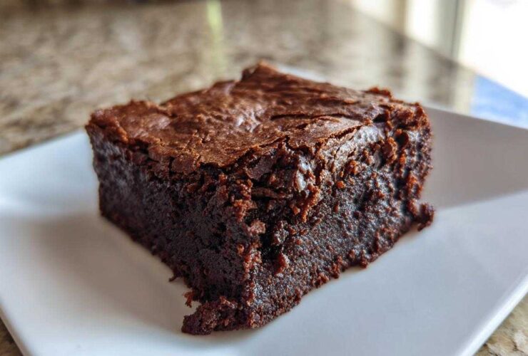 A close-up of a fudgy, rich, dark chocolate greek yogurt brownies square on a white plate.
