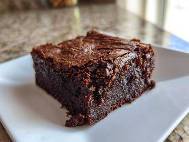 A close-up of a fudgy, rich, dark chocolate greek yogurt brownies square on a white plate.