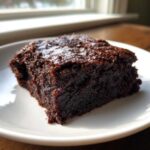 A close-up of a rich, dark, fudgy slice of Vegan Avocado Zucchini Brownies on a white plate.