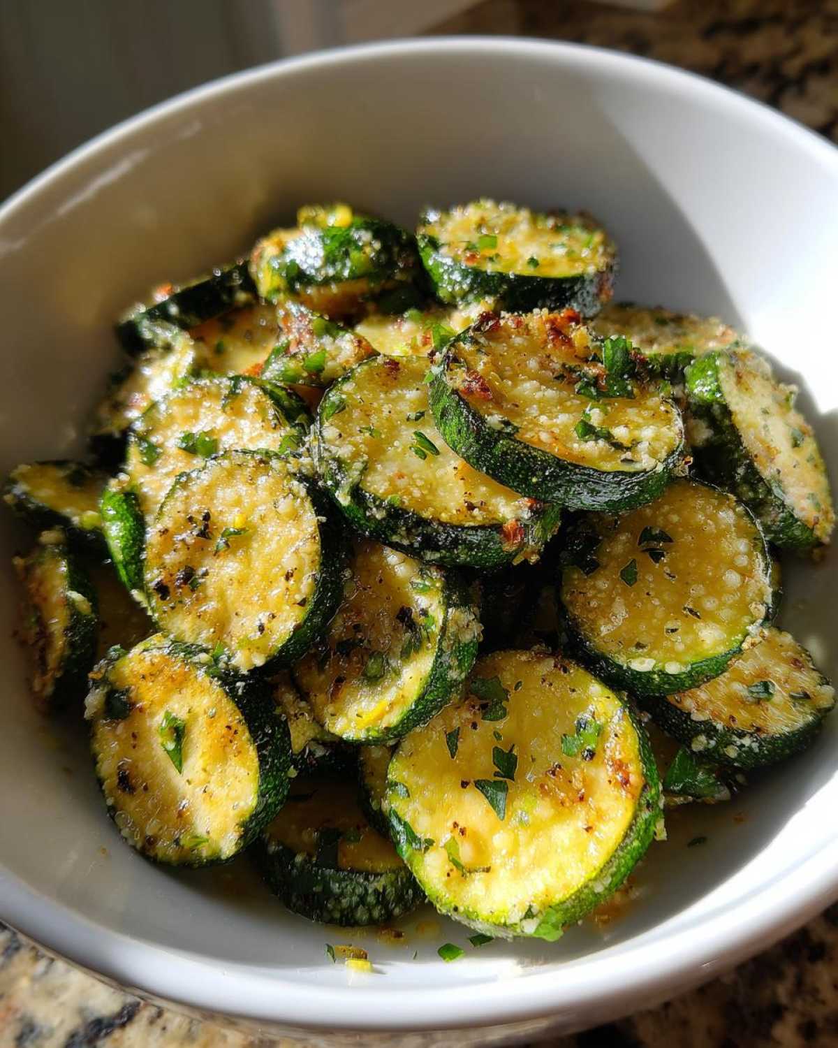 Close-up of round, sautéed zucchini slices coated in melted cheese and herbs, ready to eat as Garlic Parmesan Sautéed Zucchini.