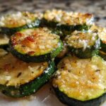 Close-up of golden brown, sautéed zucchini slices topped with minced garlic and Parmesan cheese, ready to eat.