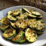 Close-up of perfectly cooked Garlic Parmesan Sautéed Zucchini slices topped with cheese and herbs.