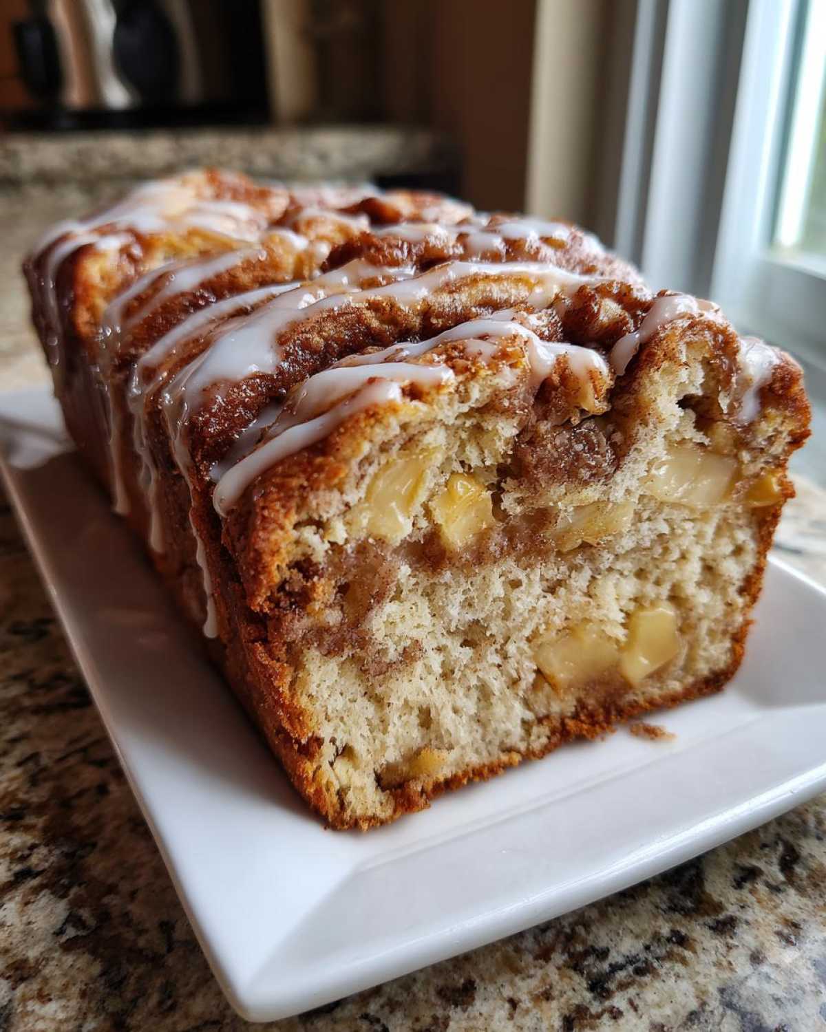 A freshly baked loaf of apple fritter bread, sliced to show chunks of apple and topped with a sweet vanilla glaze.