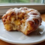 A close-up of one delicious baked apple fritters, drizzled with white icing and showing soft apple pieces inside.