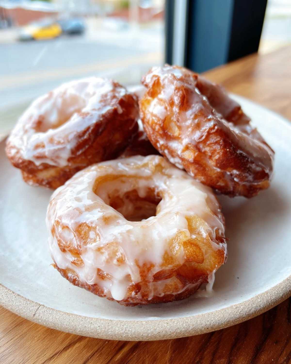 Close-up of three golden brown, glazed baked apple fritters stacked on a rustic white plate.