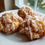 Three golden brown baked apple fritters recipe items drizzled with white glaze sitting on a white plate.