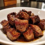 Close-up of juicy, cubed hibachi steak coated in a savory brown glaze and sesame seeds, served in a white bowl.