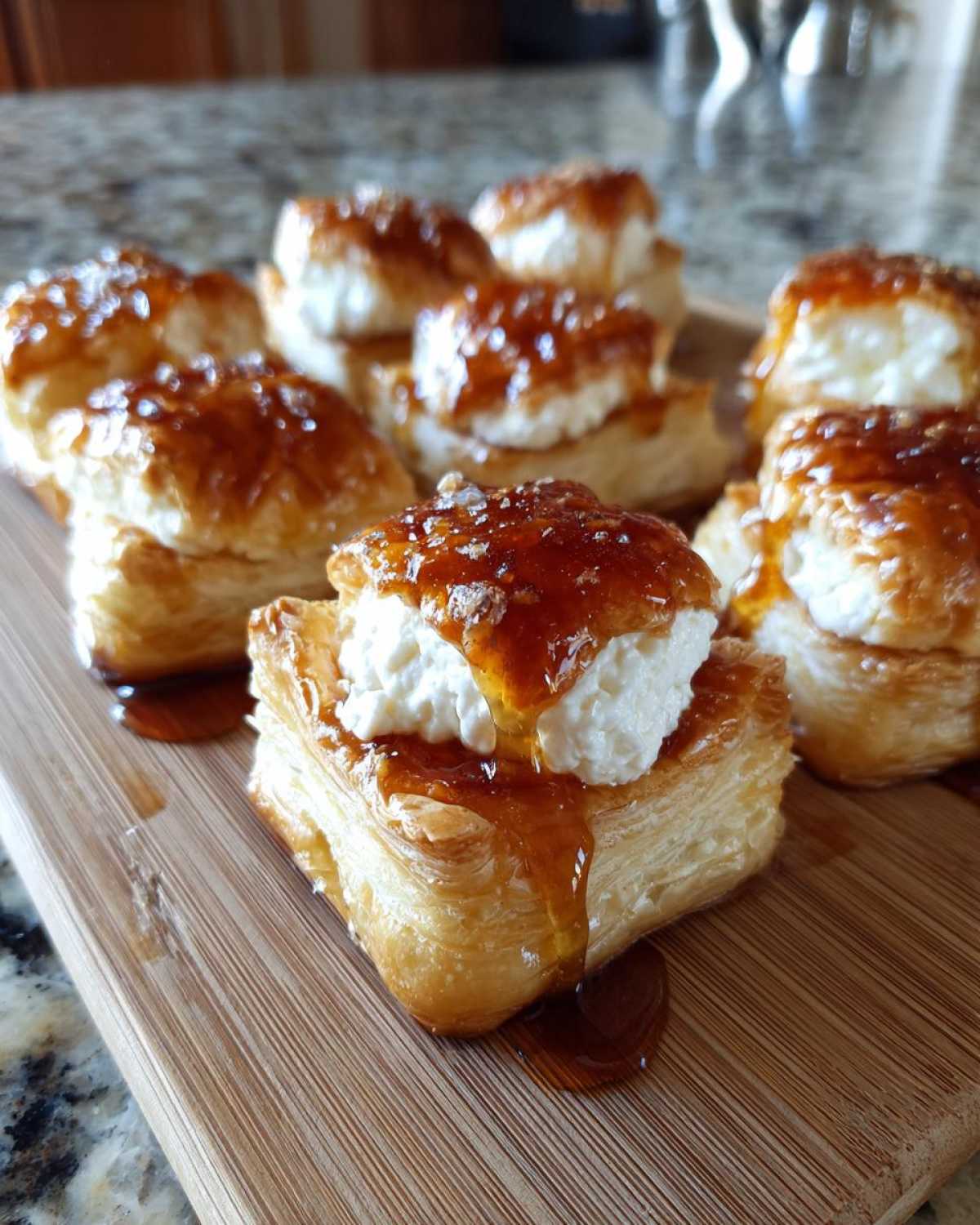 Close-up of several goat cheese and honey bites served on flaky puff pastry squares on a wooden board.