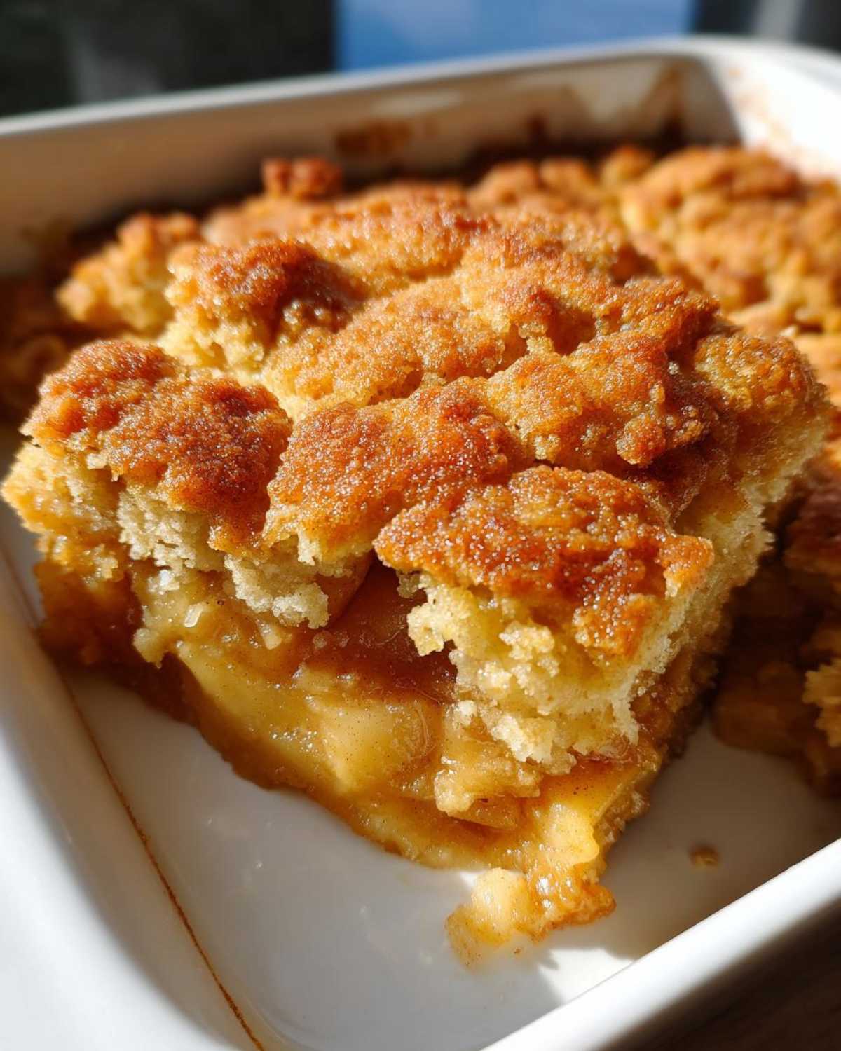 A close-up view of a serving of warm apple cobbler with a crumbly, sugary topping and gooey apple filling.