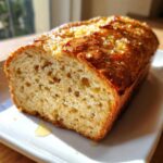 Close-up of a freshly baked loaf of beer bread with a golden, slightly crystallized top, resting on a white plate.