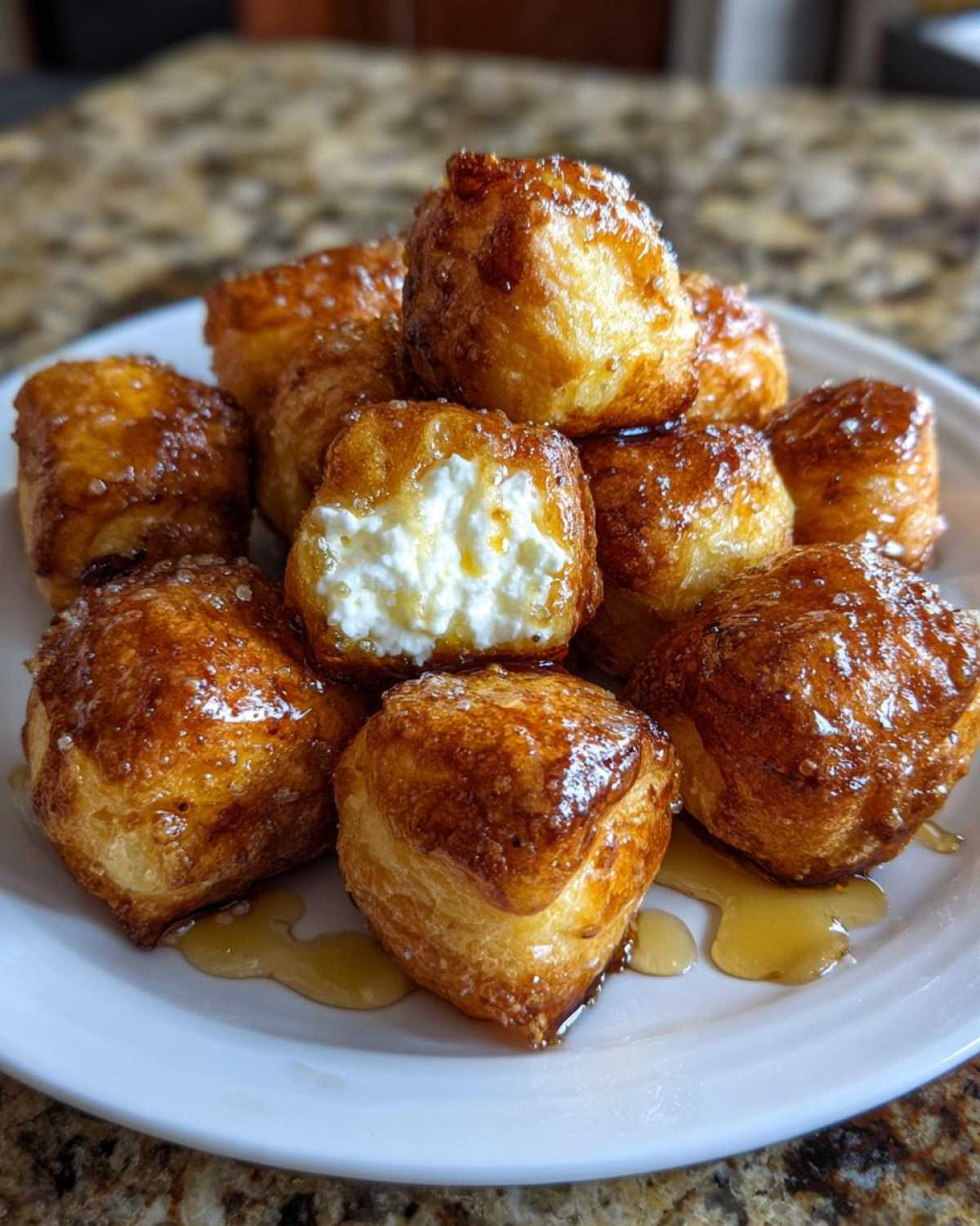 A stack of golden, fried goat cheese and honey bites, with one showing the creamy white goat cheese filling.