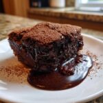A rich, dark slice of chocolate cobbler oozing with fudge sauce, dusted with cocoa powder.