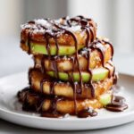A stack of four gourmet Caramel Apple Slices layered with green apple rings, drizzled heavily with chocolate sauce and sea salt.