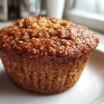 Close-up of a single, golden-brown Healthy Apple Zucchini Muffins with a slightly textured, glistening top.