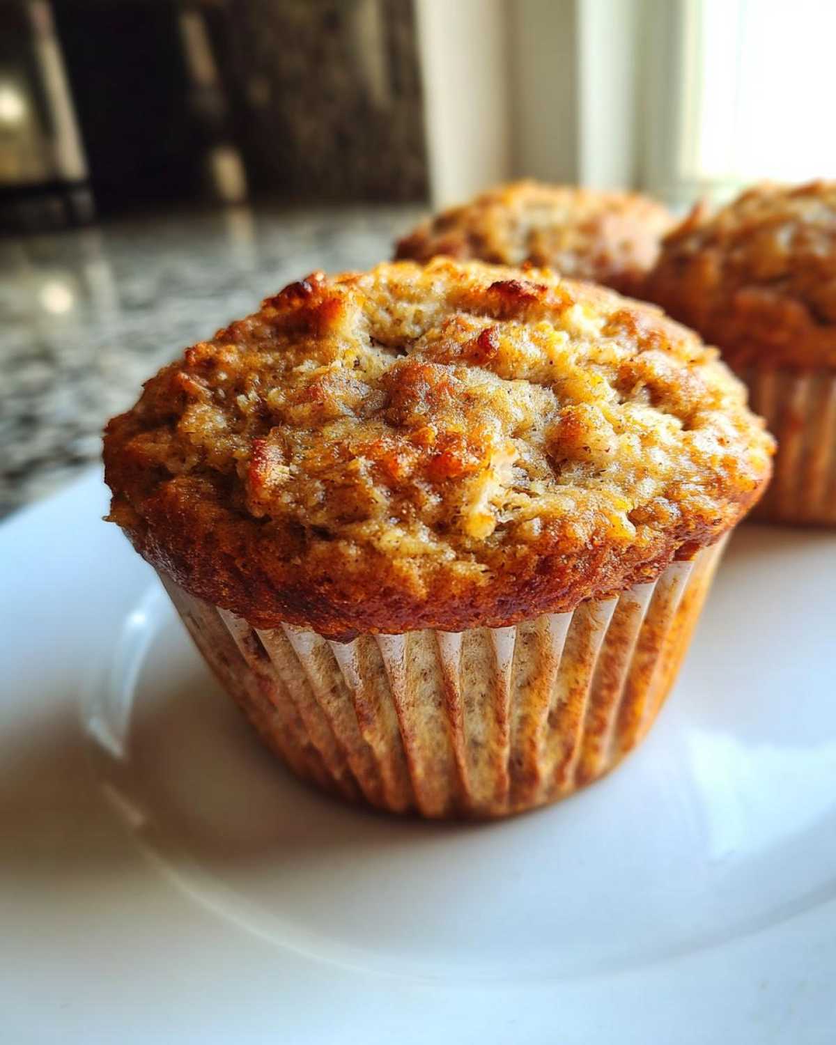 Close-up of a perfectly baked, golden-brown Healthy Apple Zucchini Muffins sitting on a white plate.