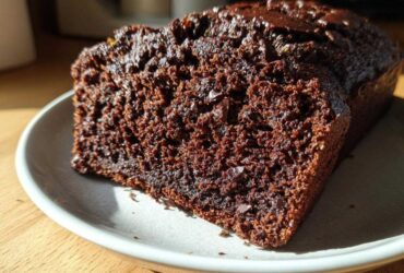 A moist, dark slice of Healthy Chocolate Zucchini Bread with visible chocolate chips on a light plate.