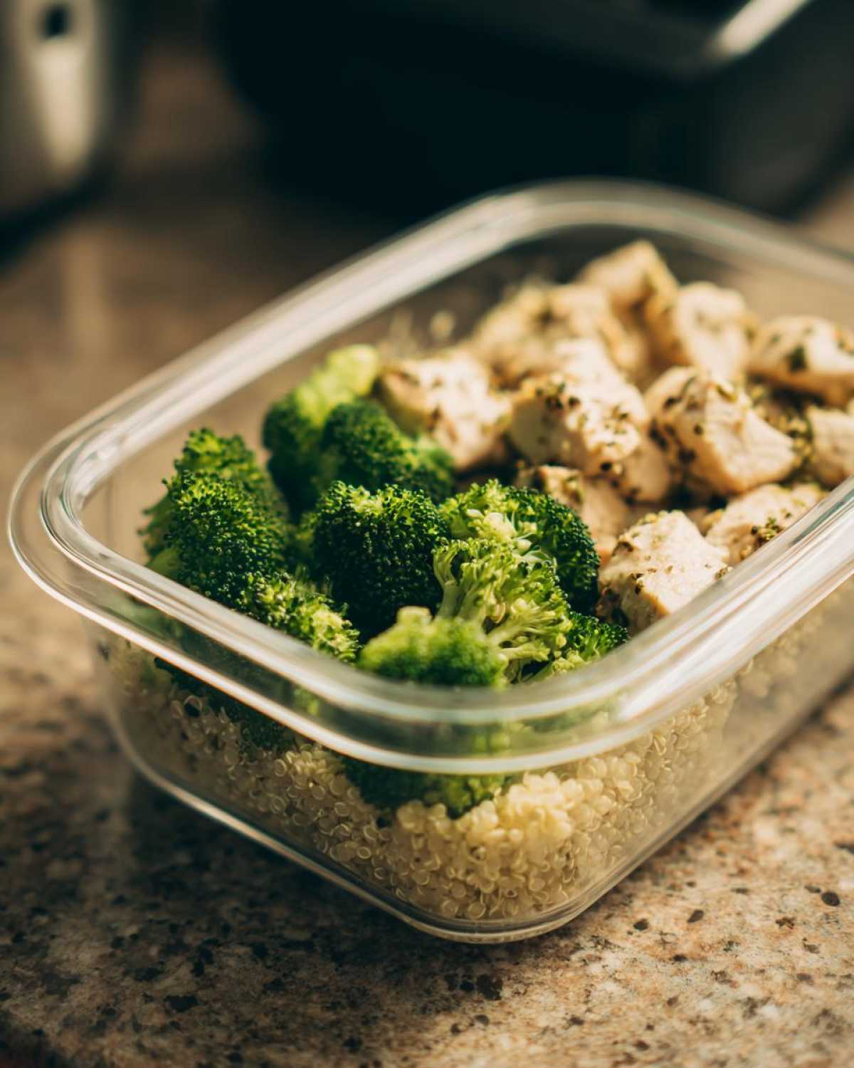 A clear container with quinoa, steamed broccoli, and seasoned chicken pieces, illustrating how you’re eating healthy wrong for busy people.
