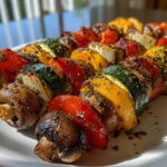 Close-up of several perfectly cooked, herb-marinated grilled vegetable skewers featuring mushrooms, peppers, zucchini, and onions.